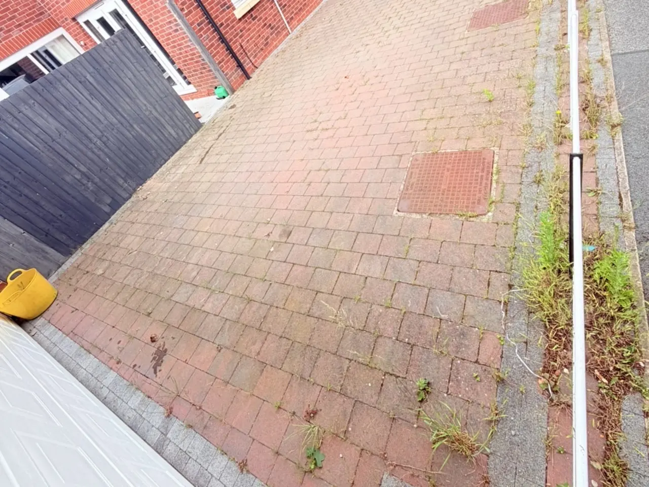 A block paving path with weeds growing through the joints and heavy staining.