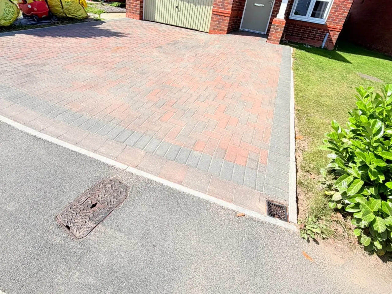 A red and charcoal block paving driveway in front of a garage after cleaning.