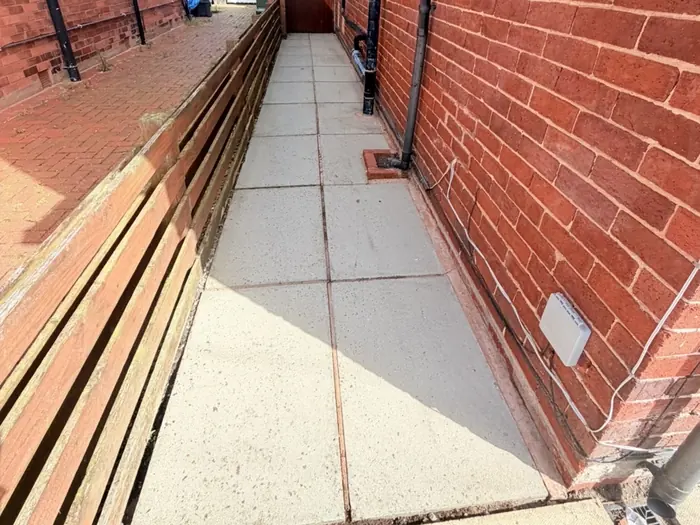 A cleaned concrete slab path running between a red brick wall and a timber fence.